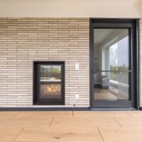 Zweiseitiger Gaskamin mit Tunnel-Tunneleinsatz, beidseitig in der Wand integriert, mit Glas auf beiden Seiten. Außenansicht vom Wohnzimmer, ideal für Terrasse oder Balkon.