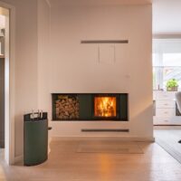 Moderner Kachelofen bzw. Kachelkamin mit verputzten Wänden, einseitig Kamineinsatz mit Umrandung aus Metall in Anthrazit.