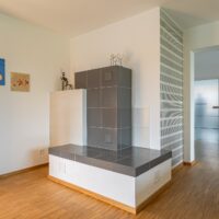 Moderner Kachelofen mit Sitzbank aus Keramik in der Ecke des Wohnzimmers.