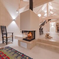 Moderner Designkamin. Kamin-Einsatz dreiseitigem Glas, Wandflächen verputzt mit Sockel aus Naturstein, passend zu den Treppenstufen.