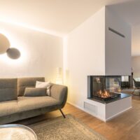 Moderner Kamin aus Naturstein, Hinterlader, dreiseitig gestaltet als Raumtrenner zwischen Wohnzimmer und Esszimmer.