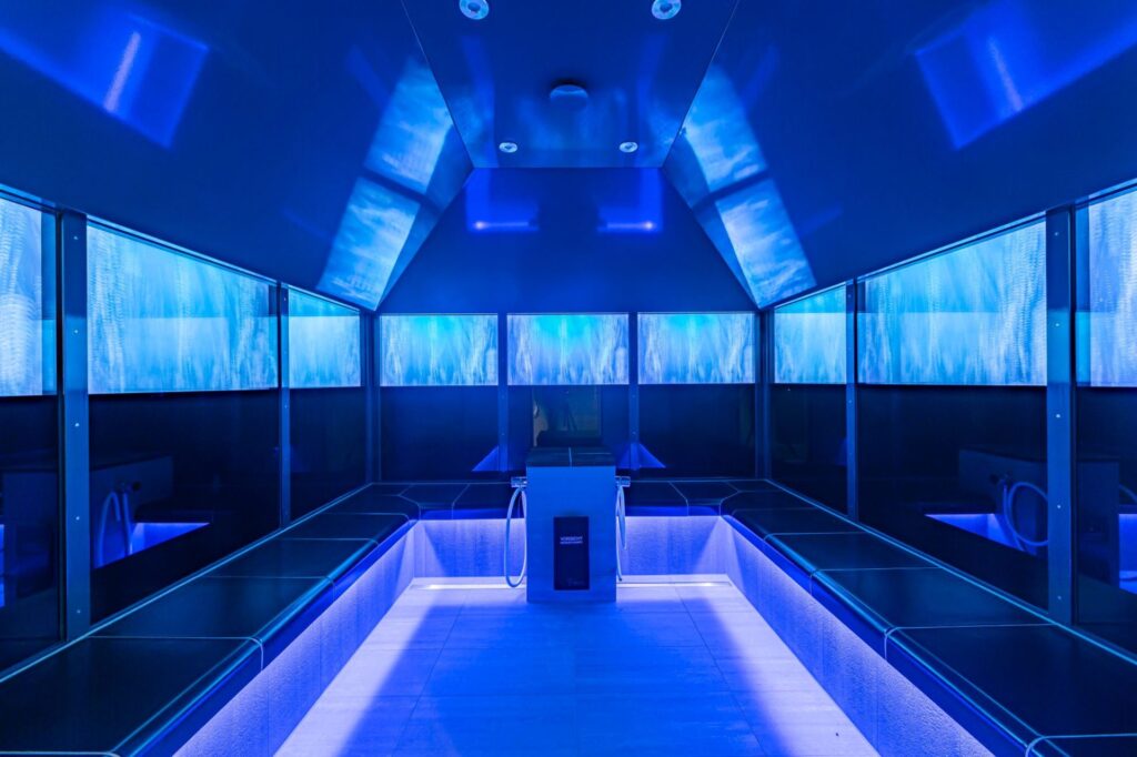 Ein Band aus Monitoren wirkt im Dampfbad von „GochNess“ wie ein Blick durch ein Panoramafenster und inszeniert Blicke in die Natur oder Unterwasserwelten. Im Zusammenspiel mit der emporragenden Decke entsteht der Raumeindruck eines Pavillons. Hygienische Sitzflächen und eine durchdachte Deckenkonstruktion leiten Kondenswasser ab.